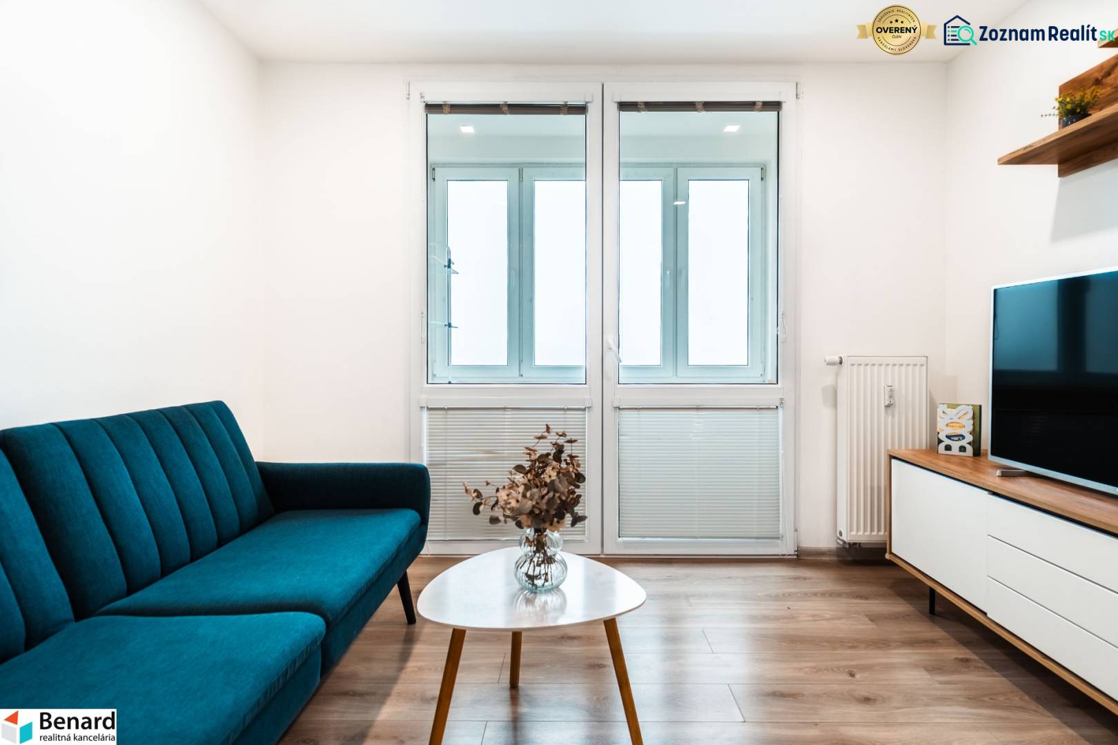 Living room in a two-room apartment with a sofa, television, and wooden decor flooring.