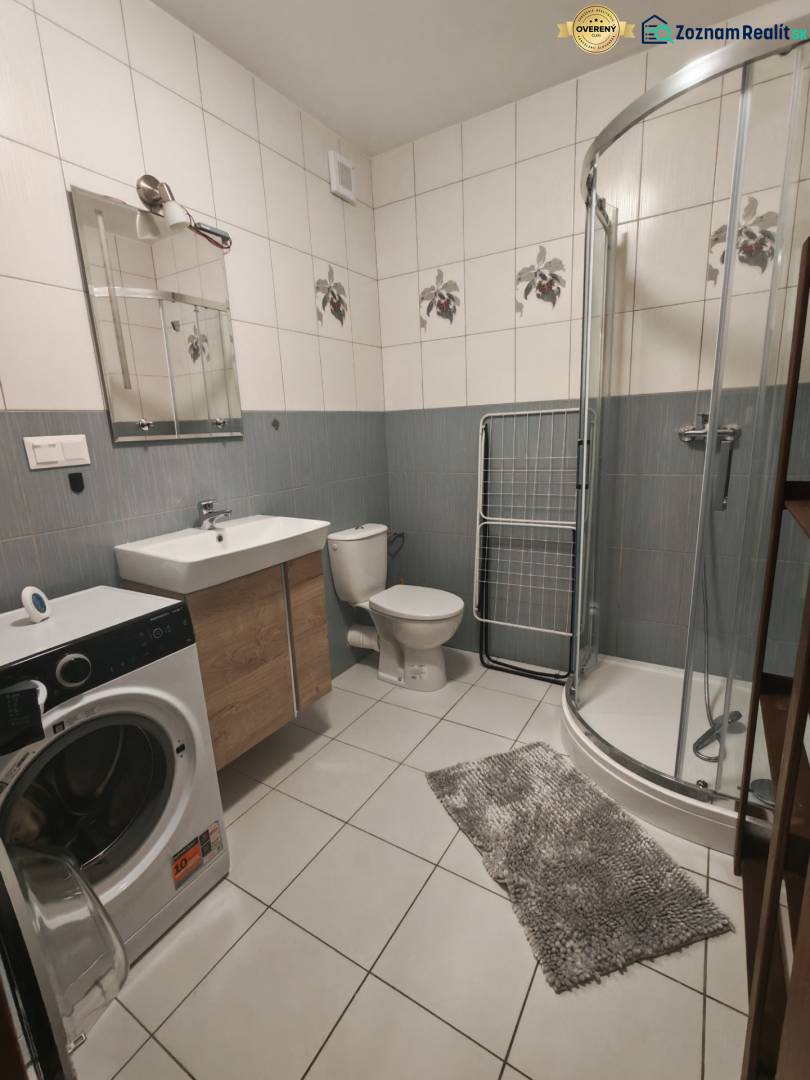 A bathroom in a 3-room apartment with a washing machine, shower corner, and ceramic tiles.