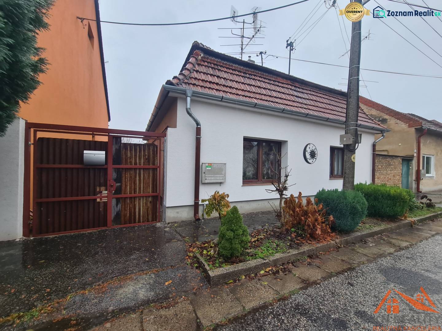 A family house in Komárno with a gable roof and an entrance gate, a front garden with shrubs.