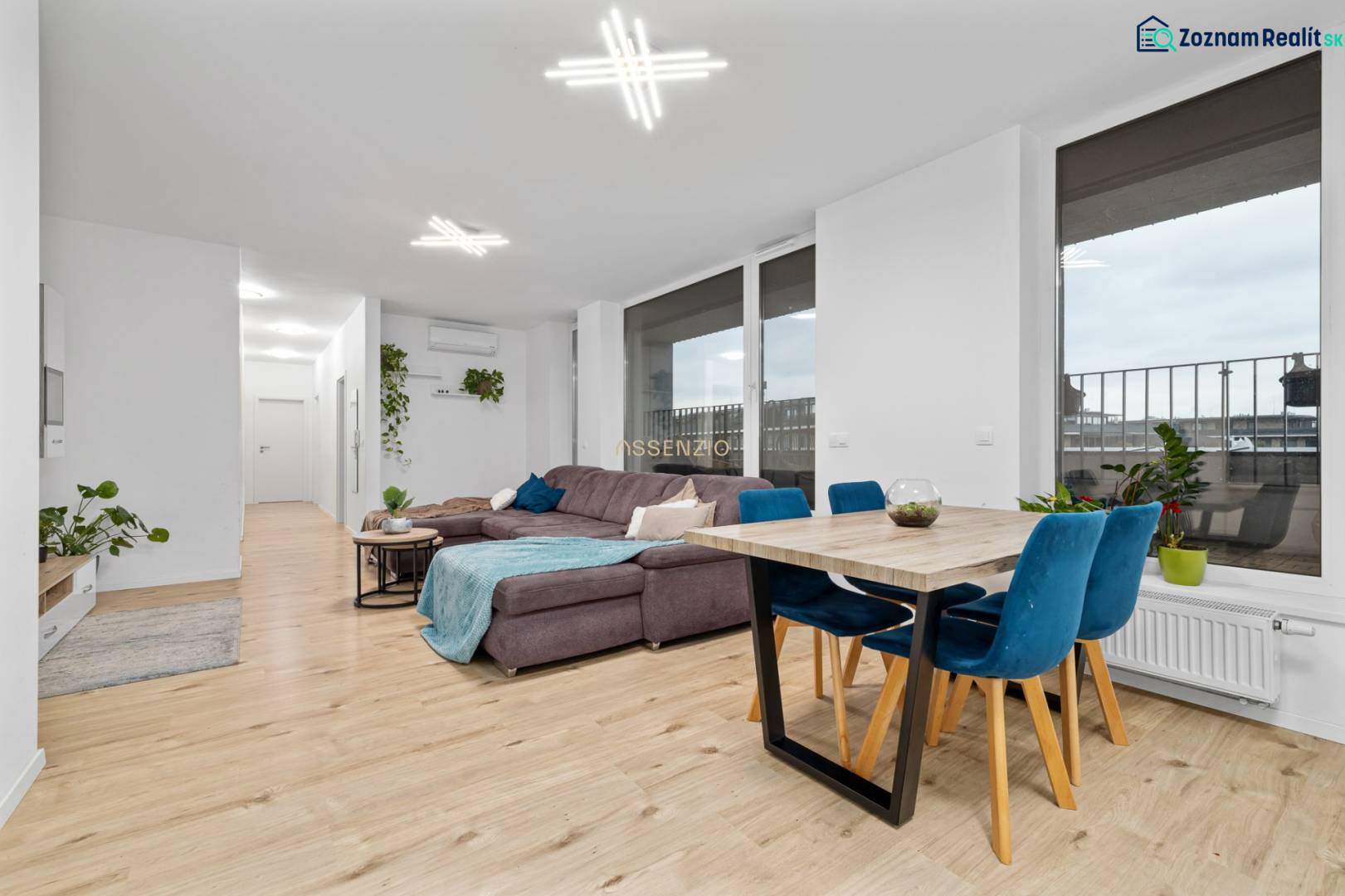 Living room in a three-room apartment with a wooden decor floor, a large sofa, and a dining table.