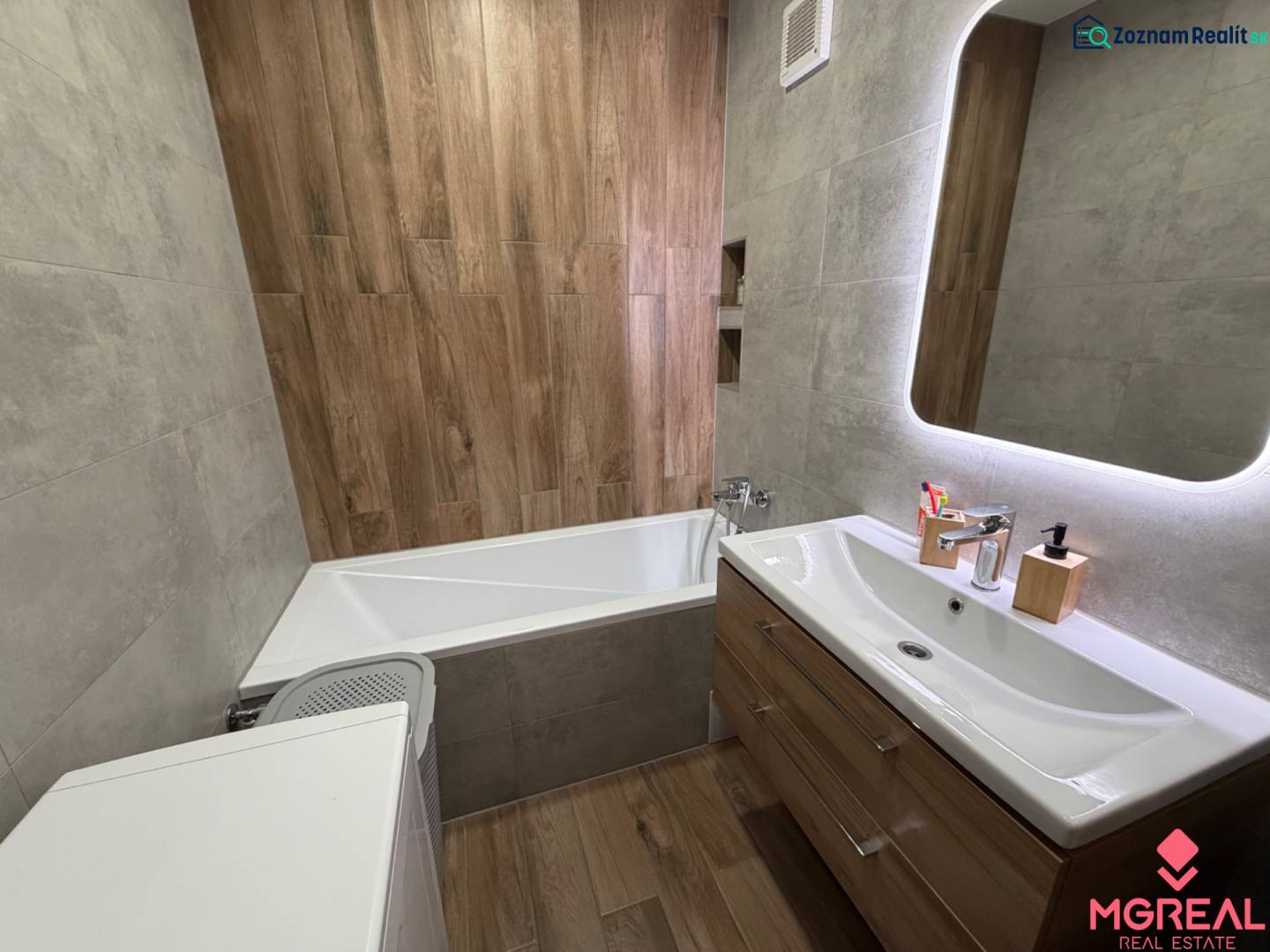Bathroom with a mirror, bathtub, sink, and floor with a wooden decor in a 4-room apartment.