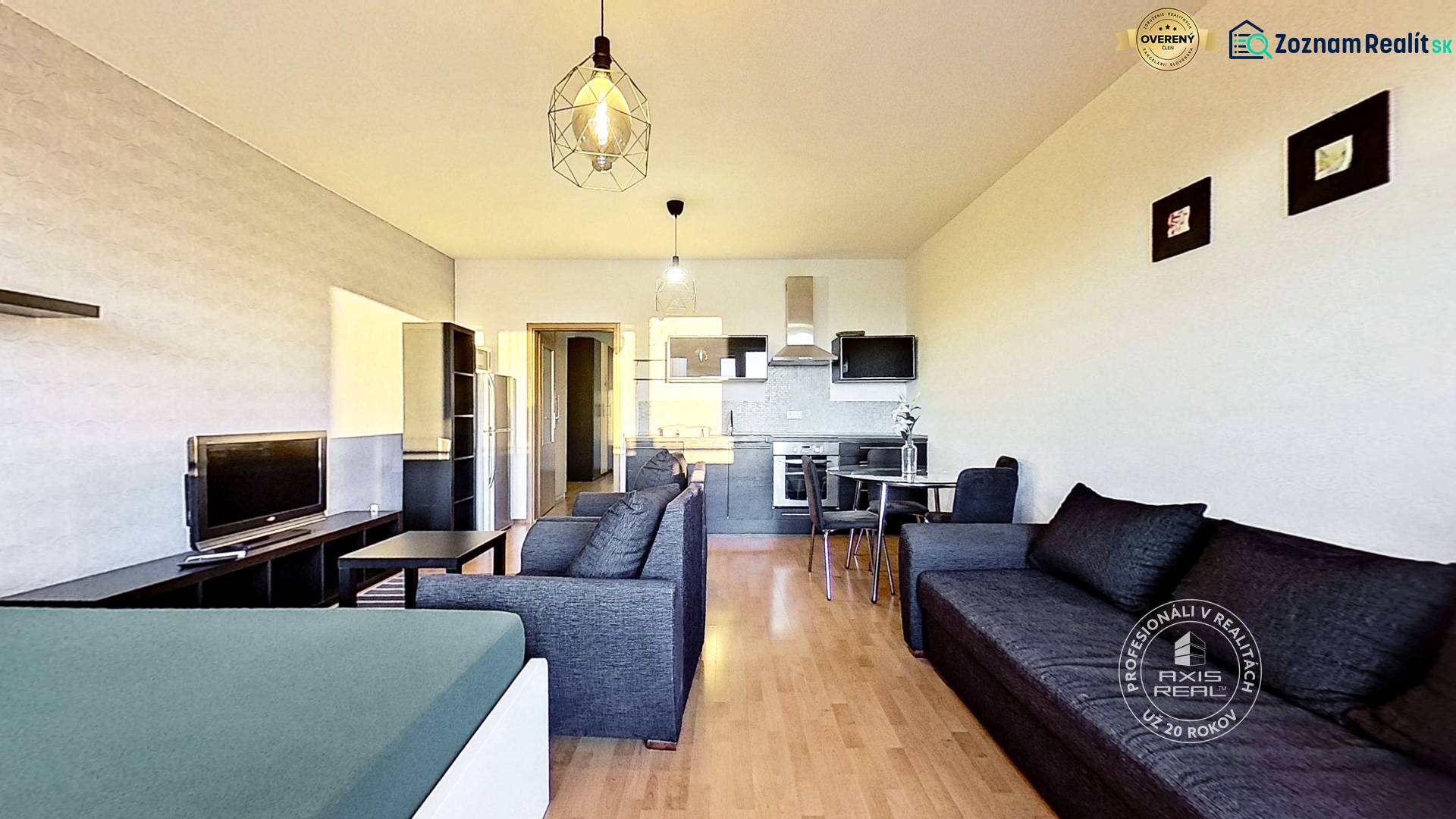 Living room in a studio apartment with a kitchen, wooden decor flooring, and dark furniture.