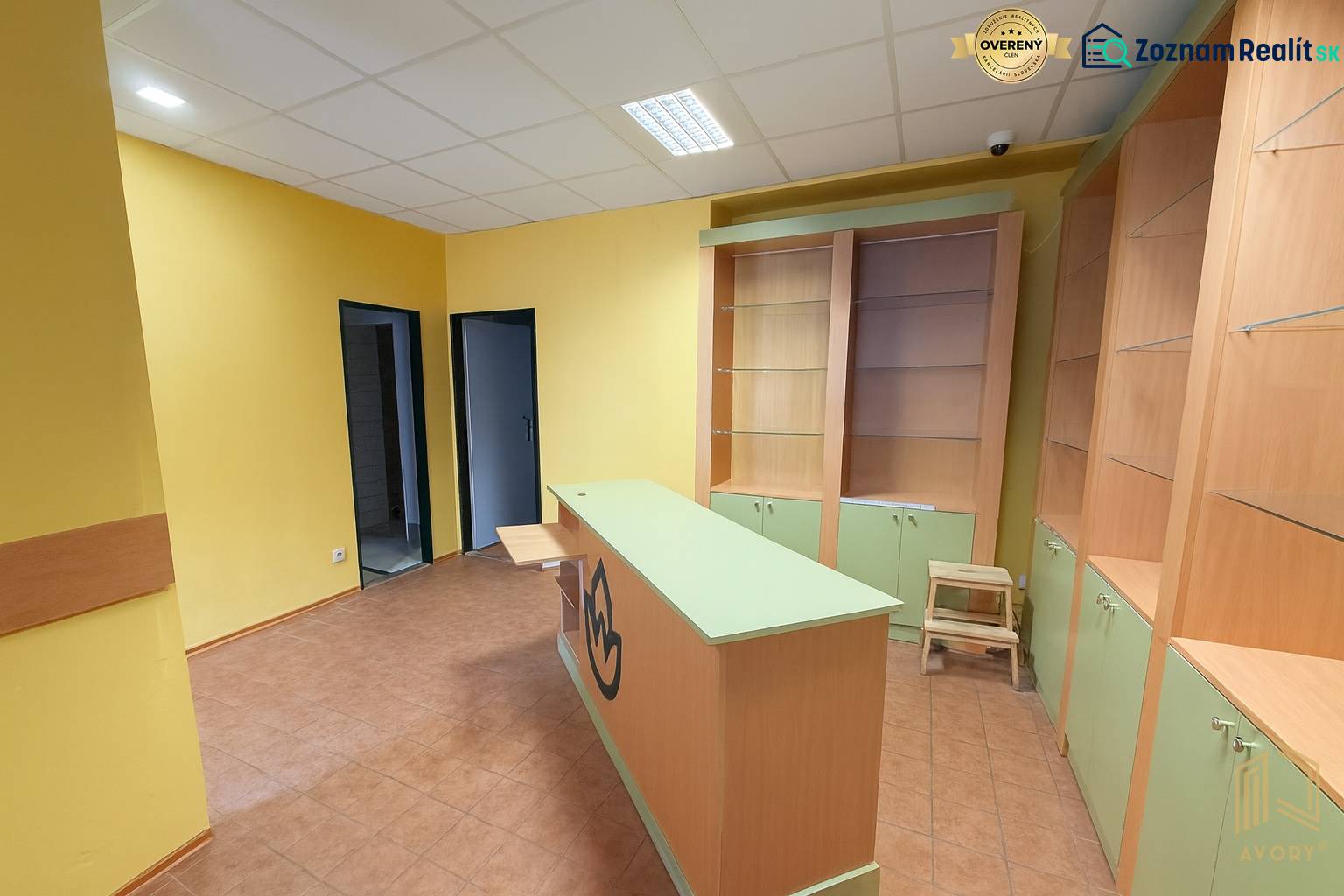 Yellow walls, counter, shelves, and tiles in commercial spaces with wood-patterned flooring.