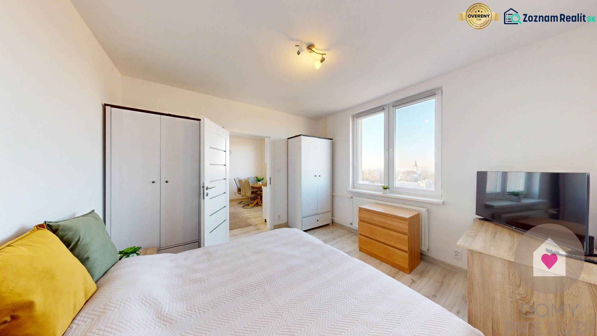 A bright bedroom in a three-room apartment with a wooden decor floor and a view of the city.
