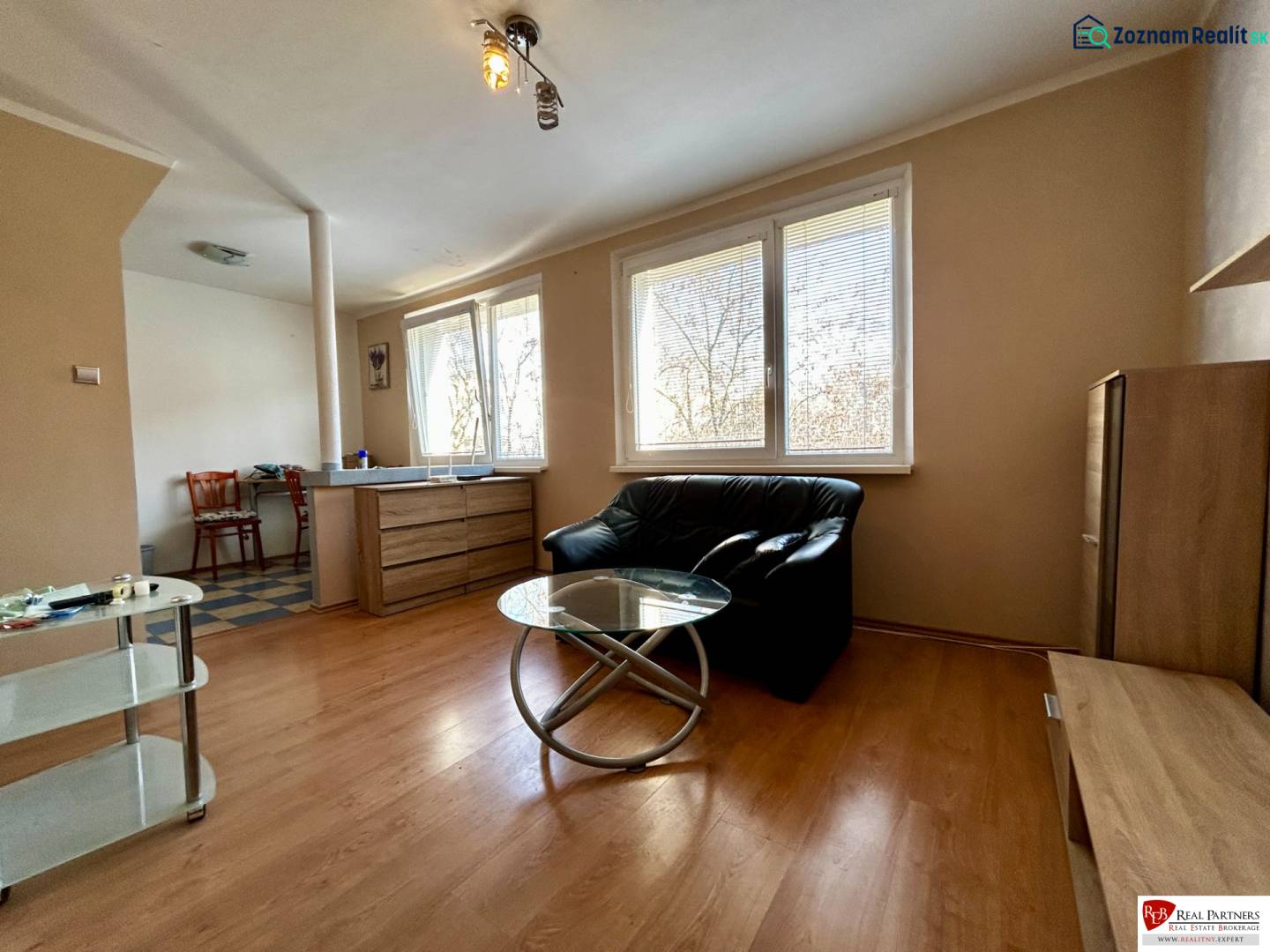 Interior of a 1-room apartment with a sofa, glass table, and wood-patterned flooring.