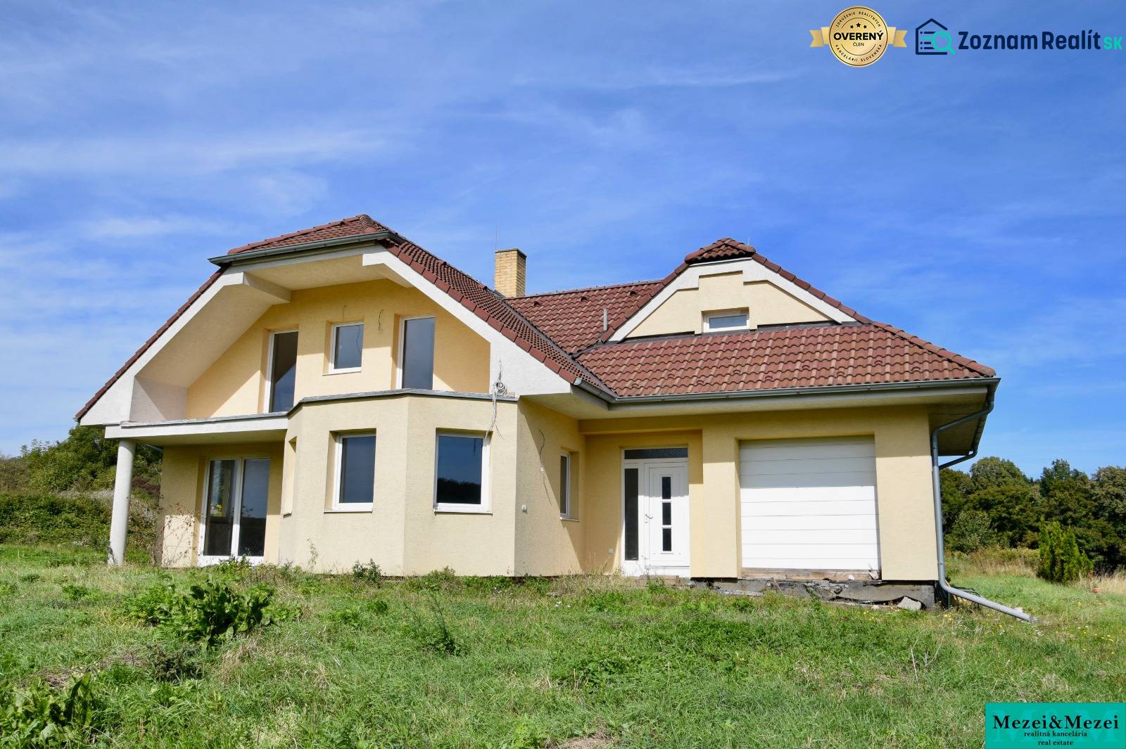 A family house in Buková with a sloped roof, light facade, and garage, surrounded by greenery.