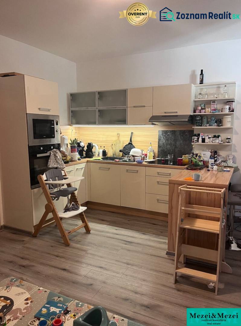 A kitchen in a 4-room apartment with a wooden decor floor, a child's chair, and toys.