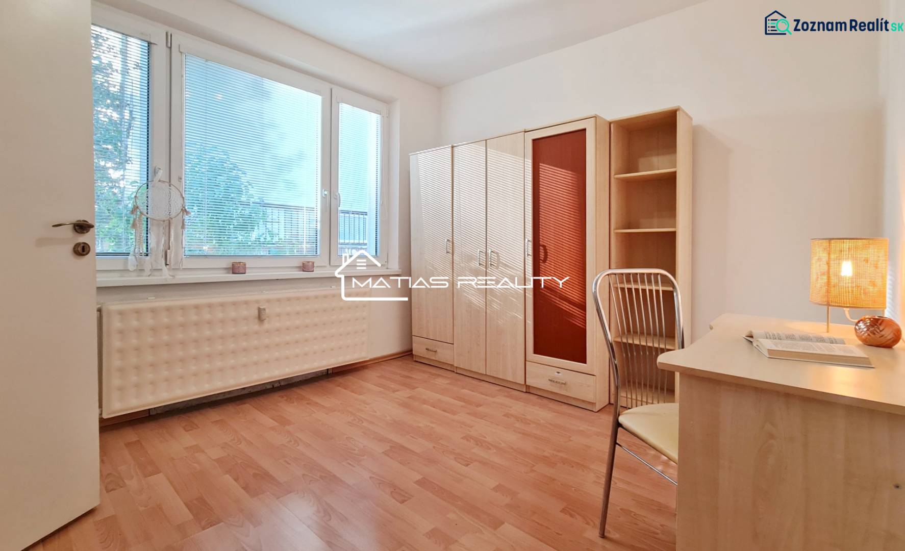 A room in a 2-room apartment with a wooden decor floor, a desk, and a wardrobe.