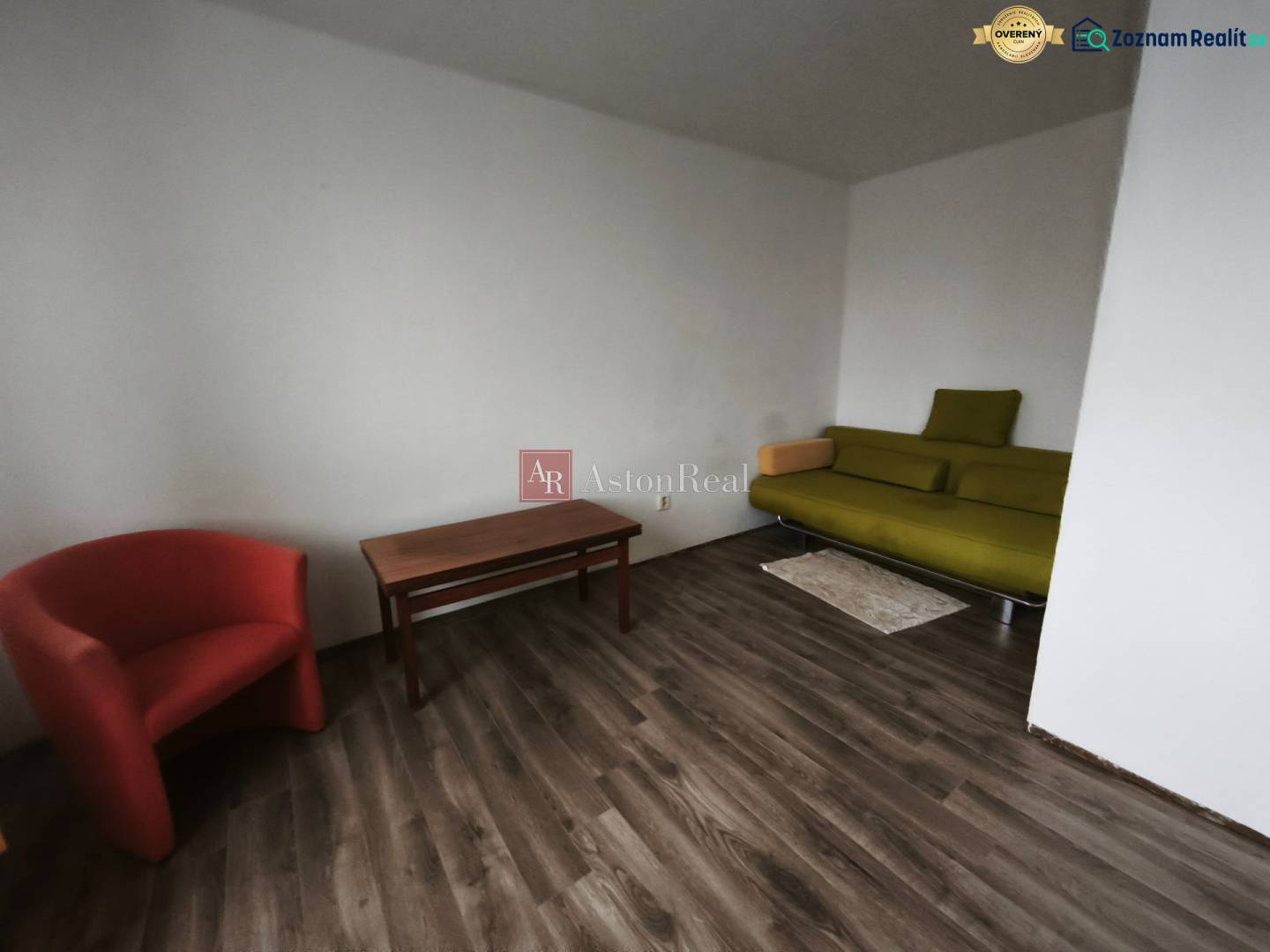 A one-room apartment with a wooden-patterned floor, a green sofa, and a red armchair.