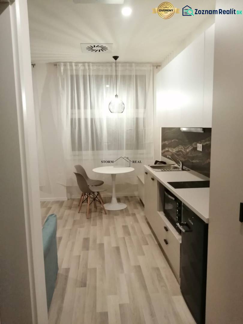 Studio apartment with wood-patterned flooring, a kitchenette, and a dining table with chairs.
