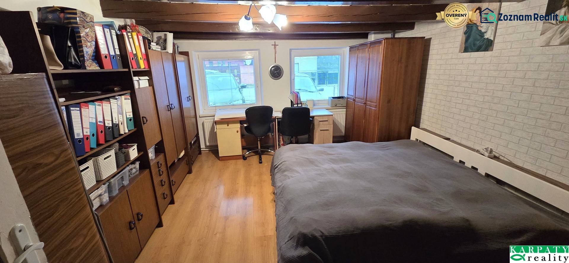 A room in a family house with a wooden decor floor, a bed, and an office corner.