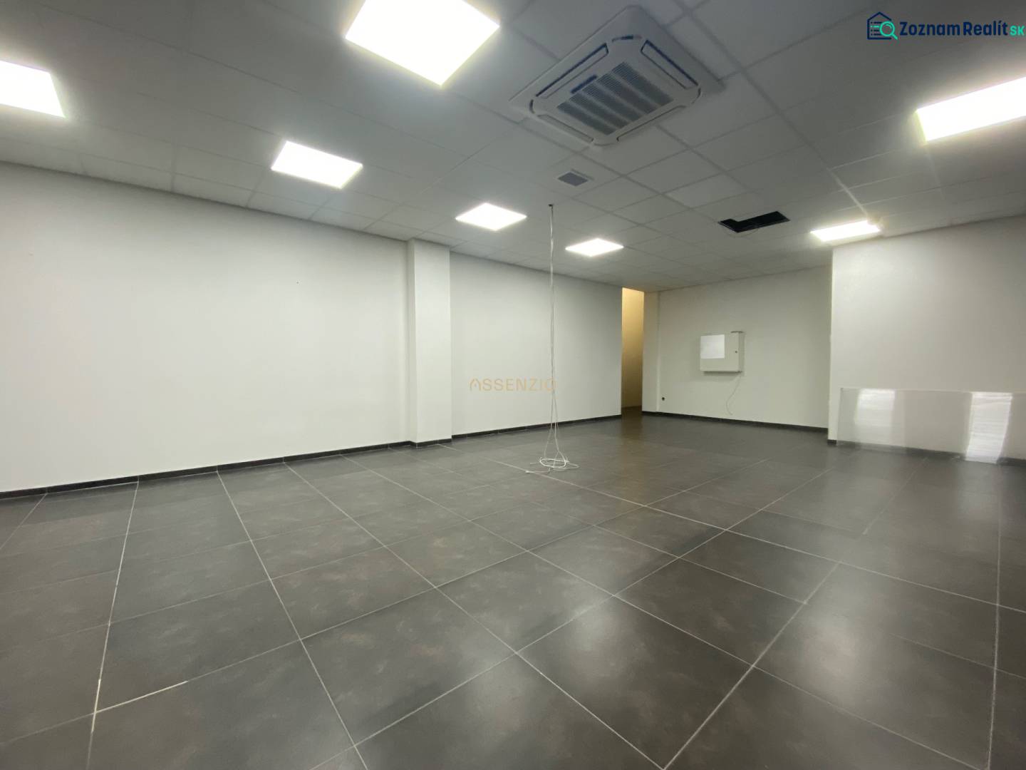 Commercial space with dark flooring and white walls, illuminated by ceiling lights.