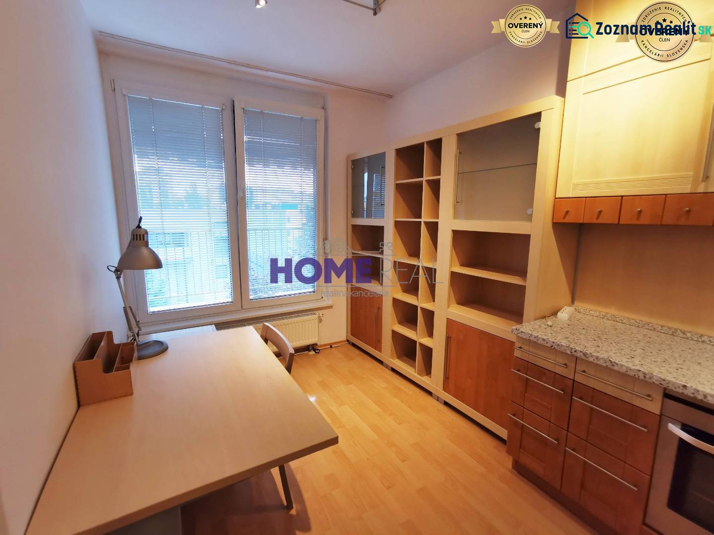 A study in a 2-room apartment with a wooden decor floor, a desk, and a bookshelf.