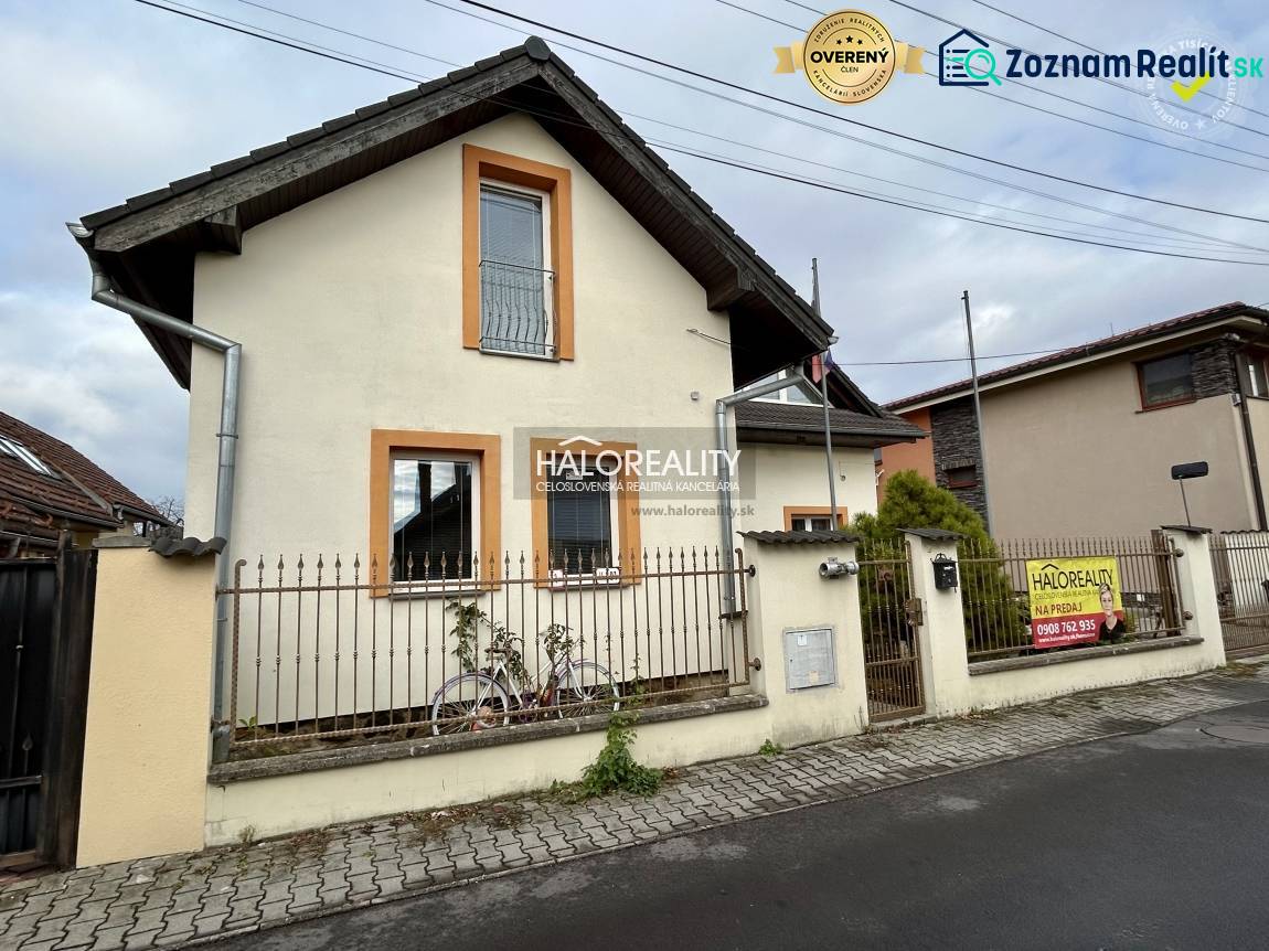 A family house in Prievidza with a fence, garden, and a real estate sign Haloreality.
