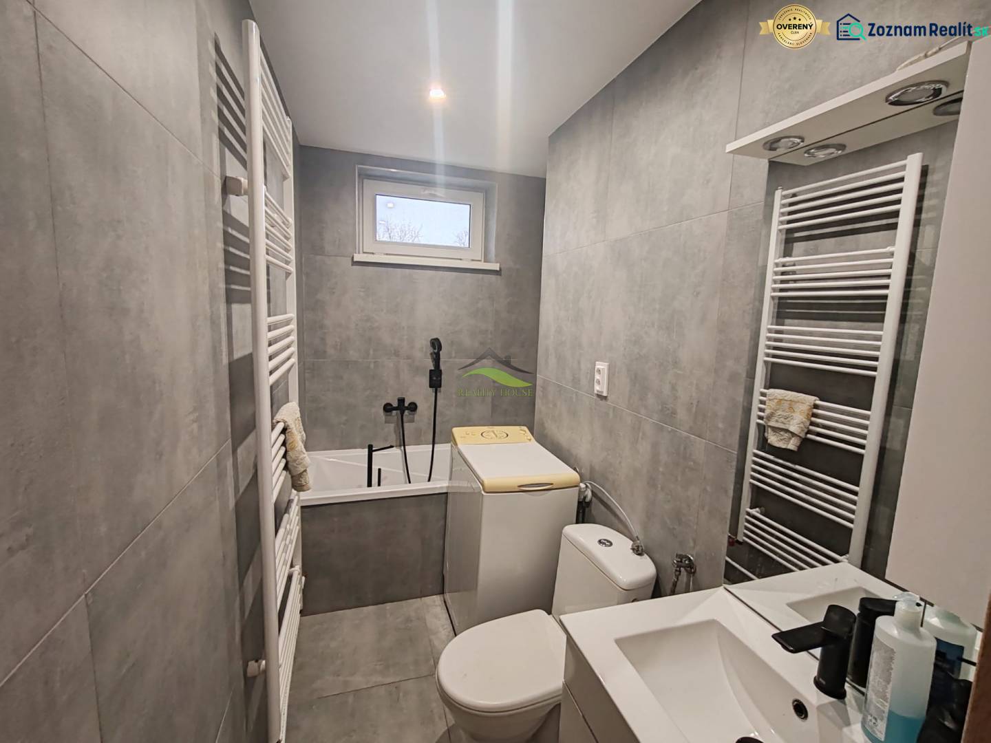 Bathroom in a 3-room apartment with a bathtub, sink, and washing machine, gray tiles.