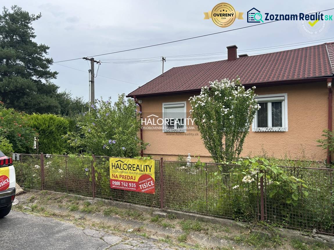 The photograph shows a family house for sale, surrounded by a green garden and a fence.