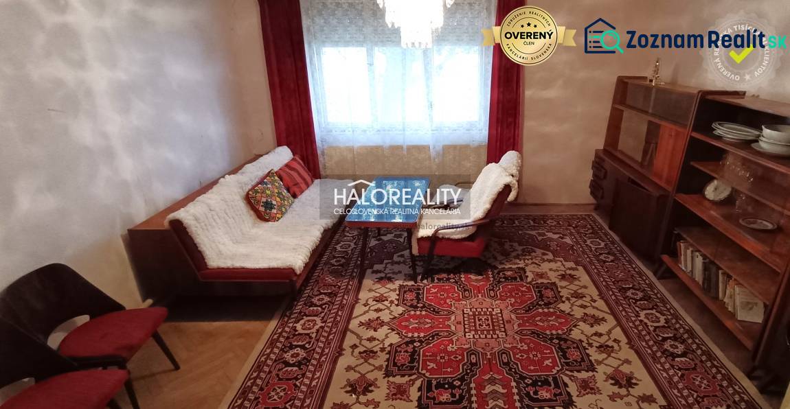 Living room with a red carpet, wooden wall unit, sofa, armchair, and cushions in a family house.