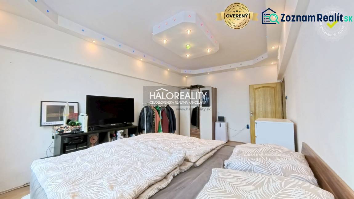 A room in a 2-room apartment with a bed, TV, and minimalist lighting.