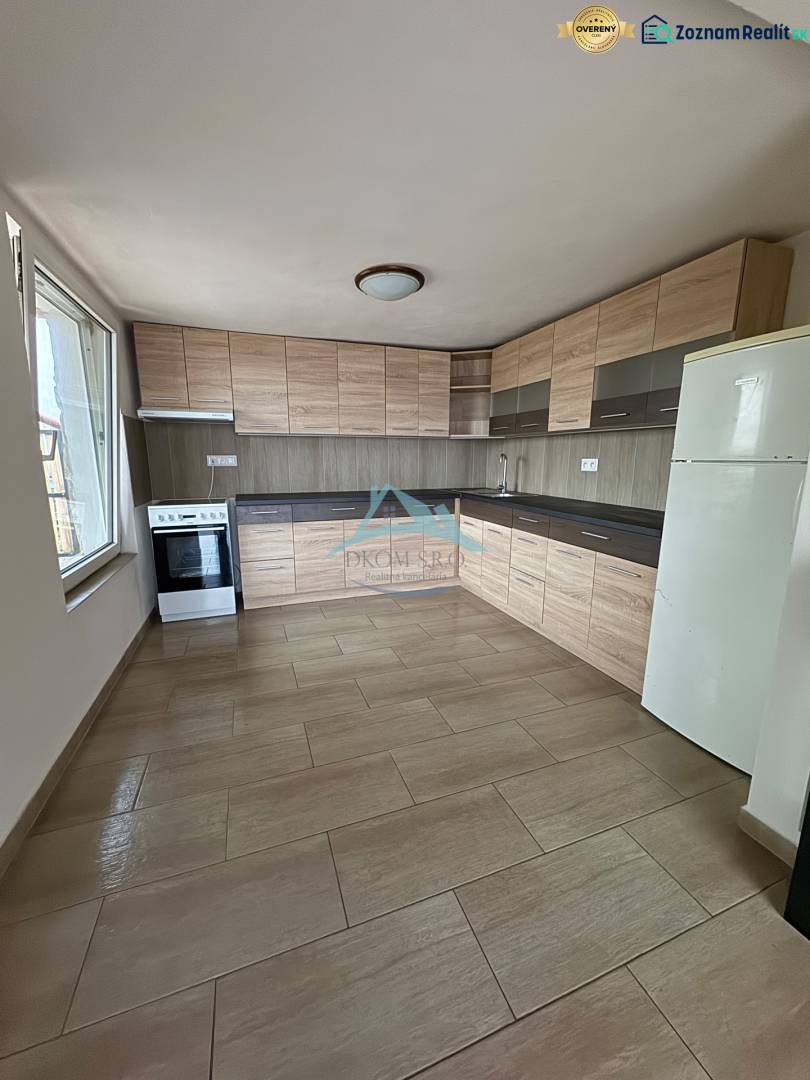 A kitchen in a cottage with light furniture, a wooden decor floor, and a large window.