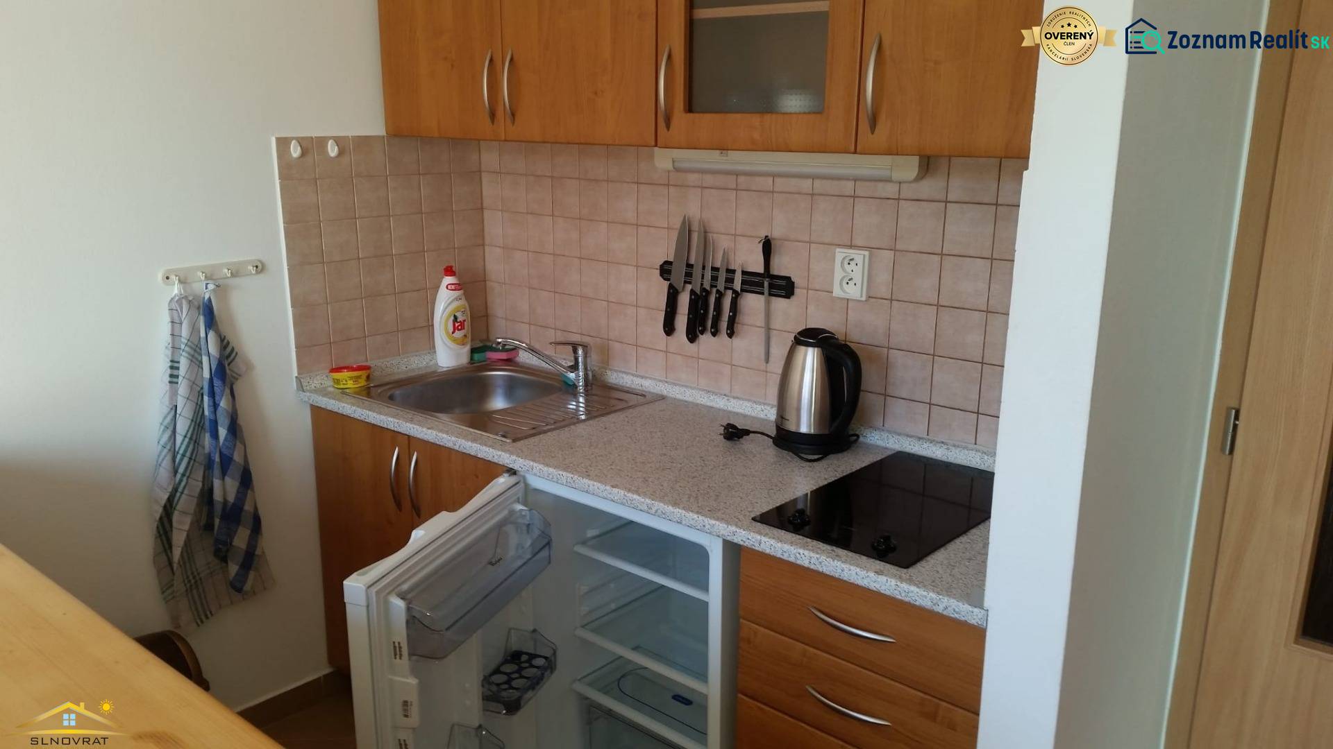 Kitchen unit with a cooktop, open refrigerator, and storage space in a recreational apartment.