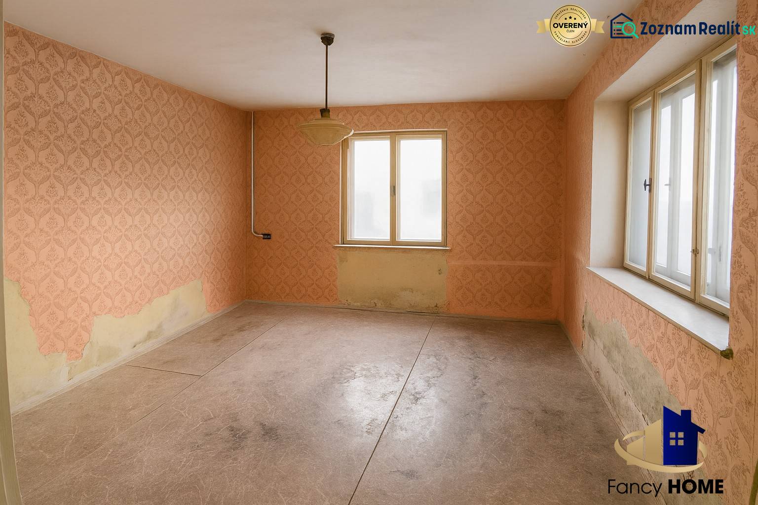 A room in a family house with peeling wallpaper on the walls and large windows.