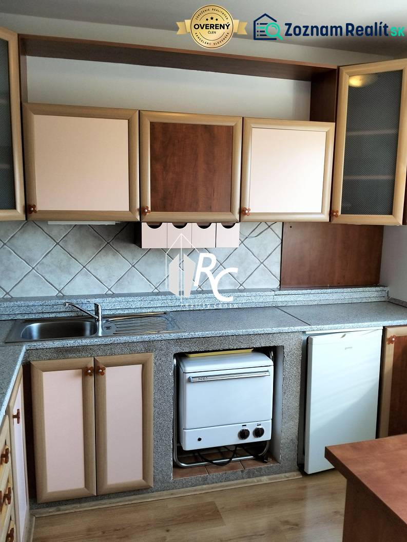 The kitchen of a one-room apartment with a wooden decor floor and a kitchen counter.