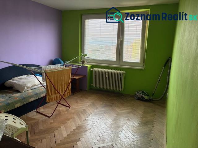 A room in a 3-room apartment with a wooden decor floor, a bed, and a clothes drying rack.