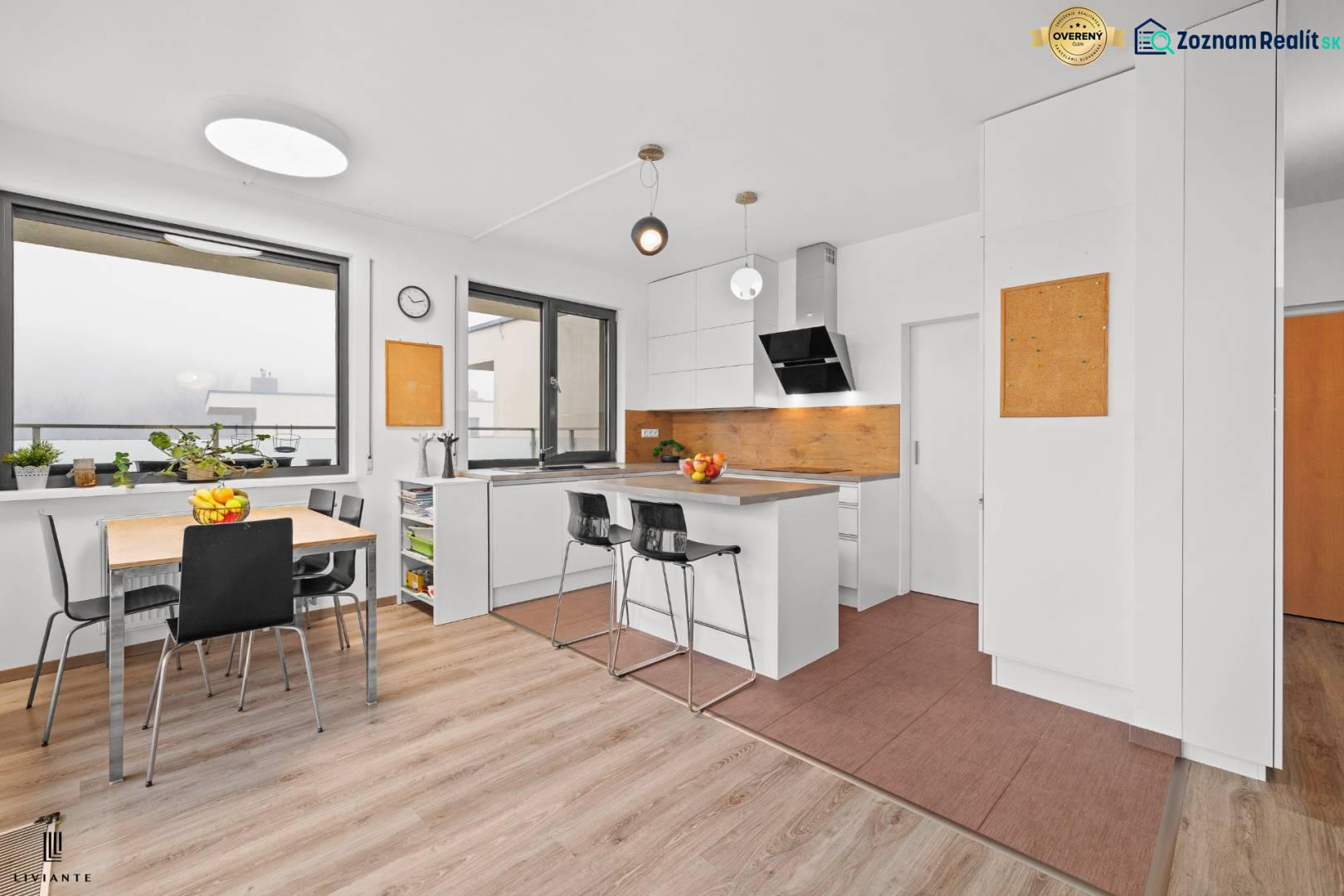 A kitchen in a 3-room apartment with a wooden decor floor, white cabinets, and a dining table.