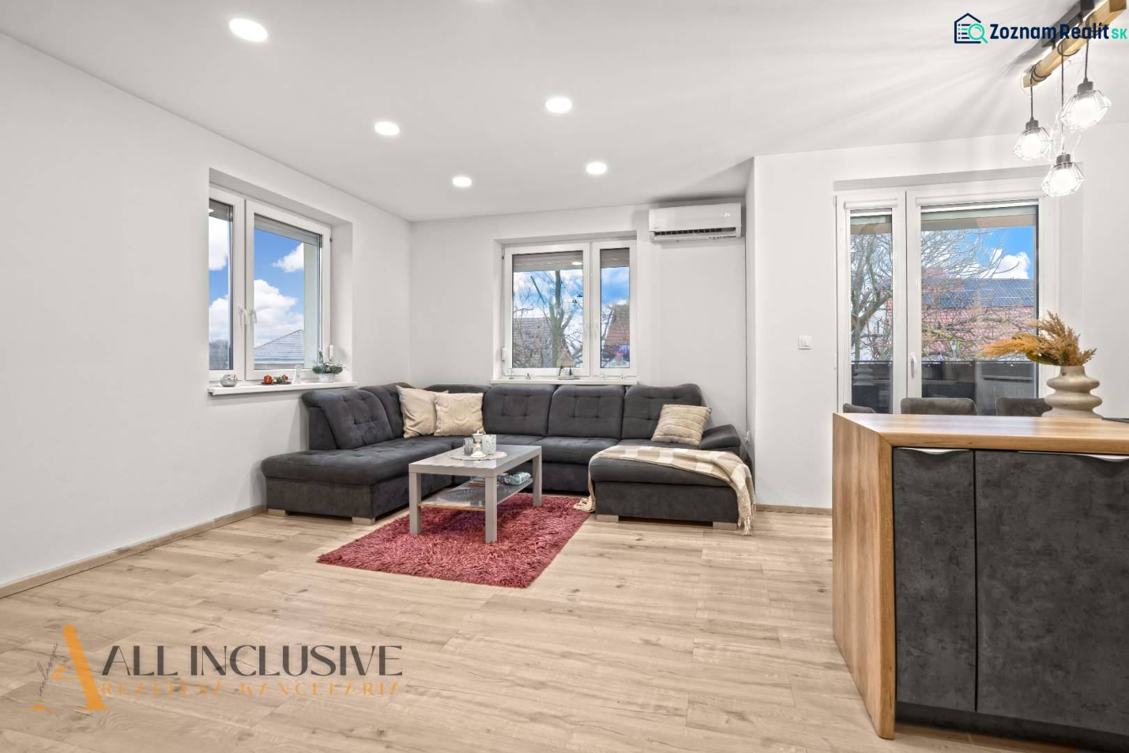 Living room of a three-room apartment with a wooden decor floor, comfortable seating, and large windows.
