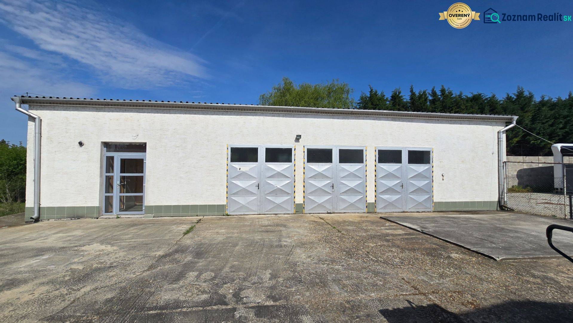 A white building with four metal gates and an entrance in Šaľa, suitable for warehouses and halls.