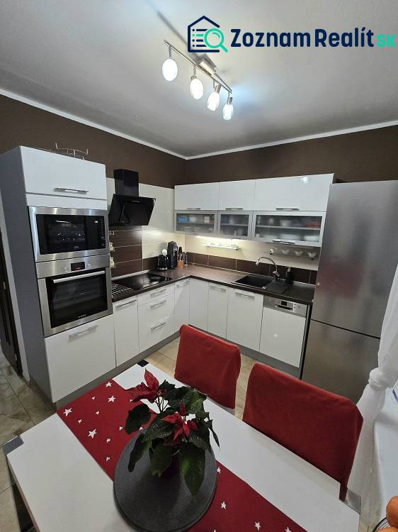 A kitchen in a 3-room apartment with white cabinets, stainless steel appliances, and decorations on the table.