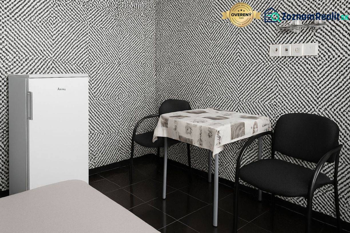 Interior with black and white patterned wallpaper, a standalone refrigerator, a table, and two chairs.