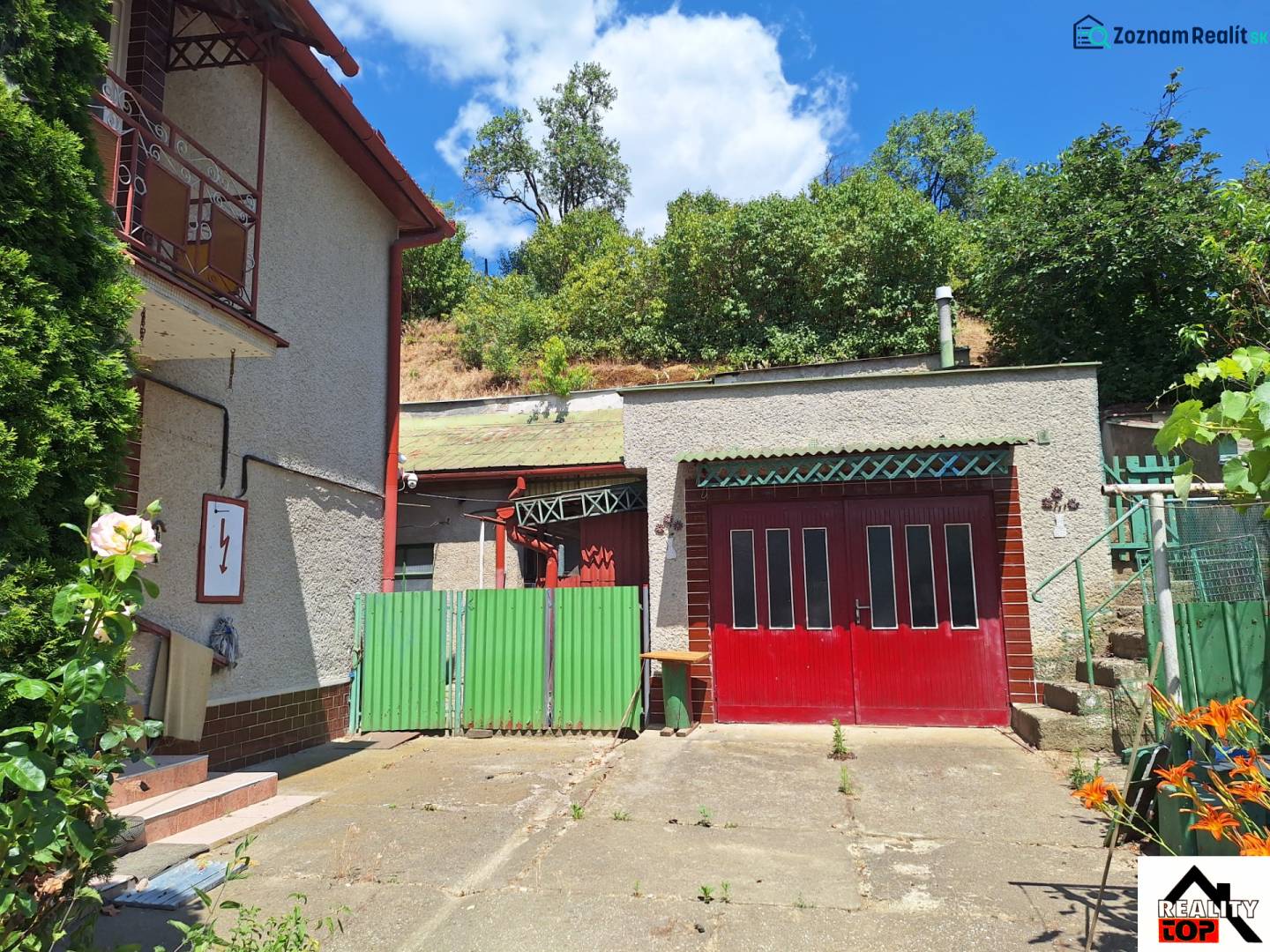 A family house in Tachtoch with an entrance gate, a garage, and surrounding greenery.