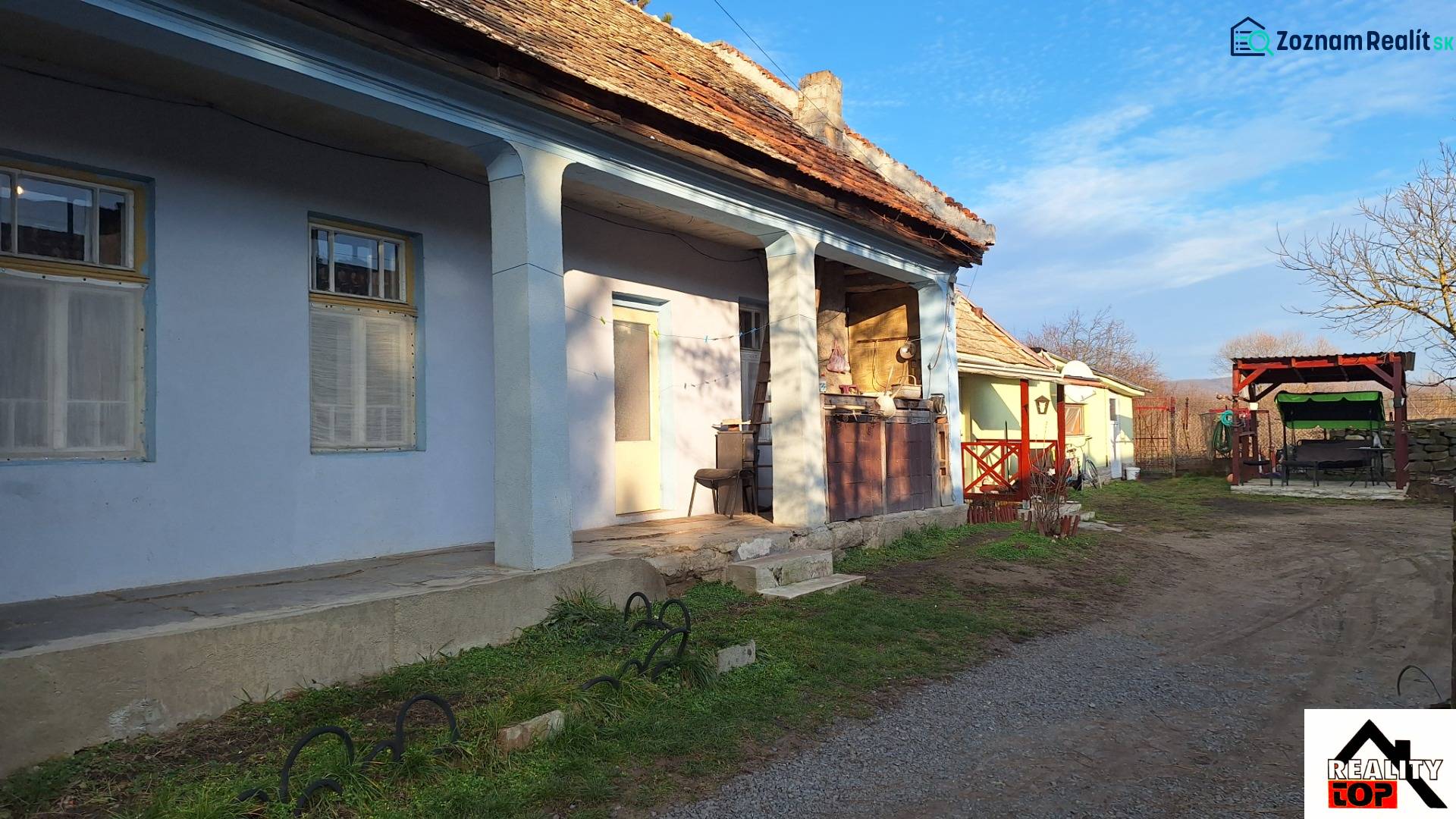 A family house in Rapovce with a blue facade and a large veranda. A yard with seating.
