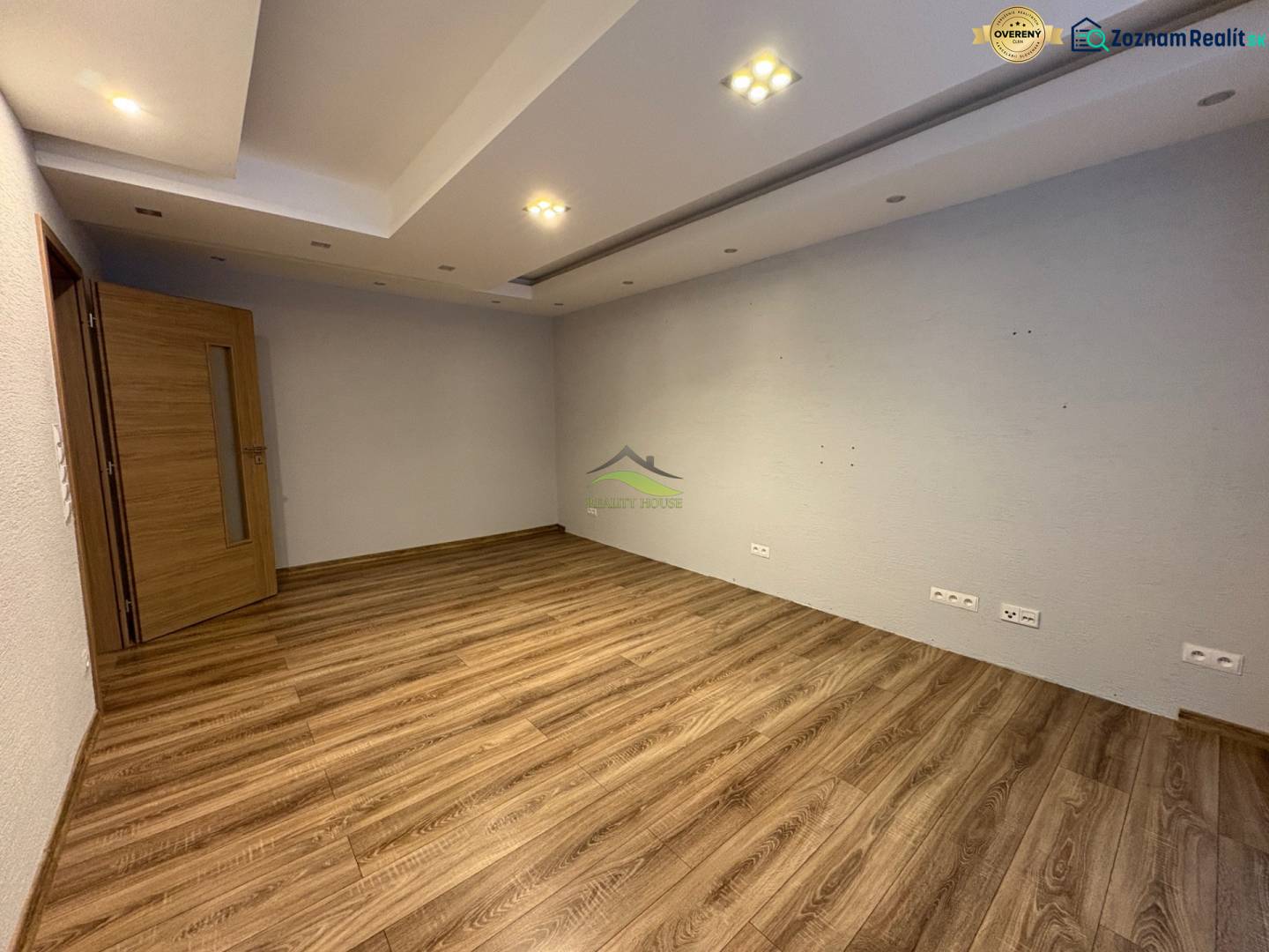 An empty room with wood-patterned flooring, white walls, and lighting in a 3-room apartment.