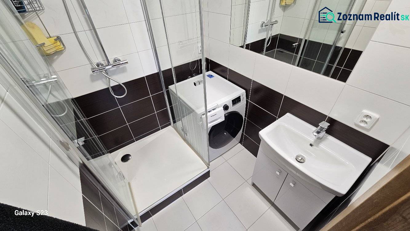 A bathroom with a washing machine, shower, and sink in a 3-room apartment.