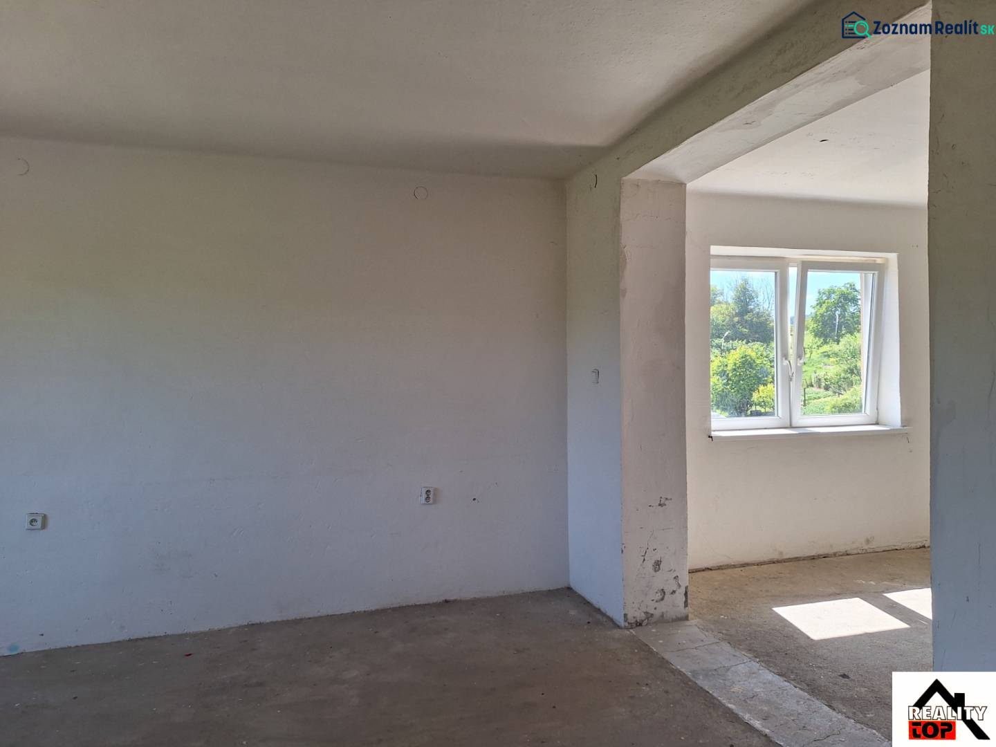 An unfurnished room in a family house with a view of the garden through a plastic window.