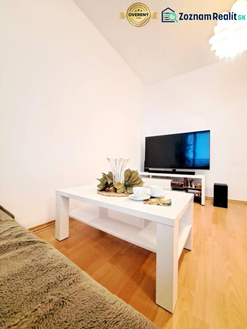 Living room in a two-room apartment with a wooden decor floor and a white table.