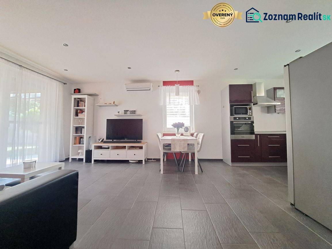 Living room with TV, kitchen, and dining table, floor with wooden decor.