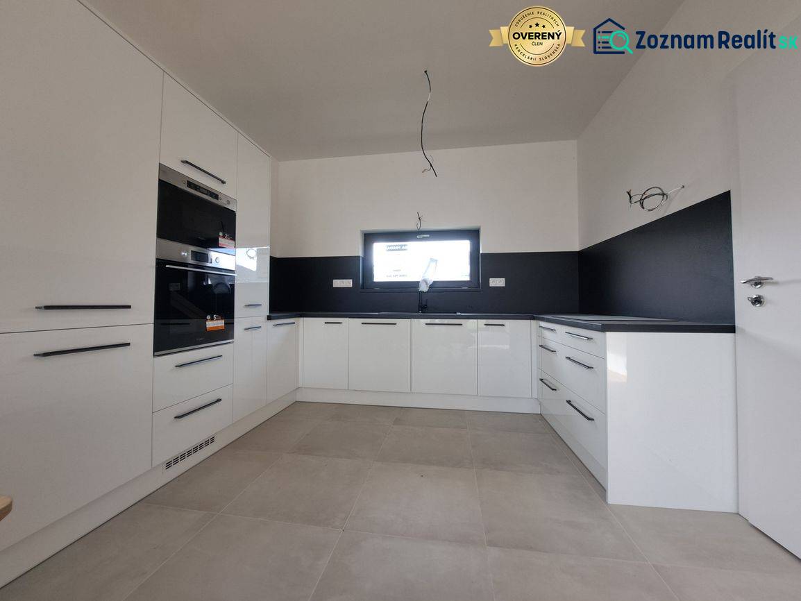 White kitchen unit and black tiles in a family house with a window and appliances.