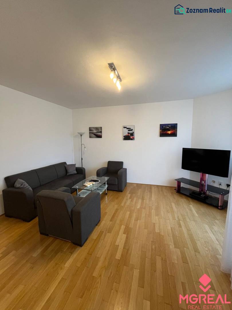 Living room in a three-room apartment with a wooden decor floor, a sofa, and a television.