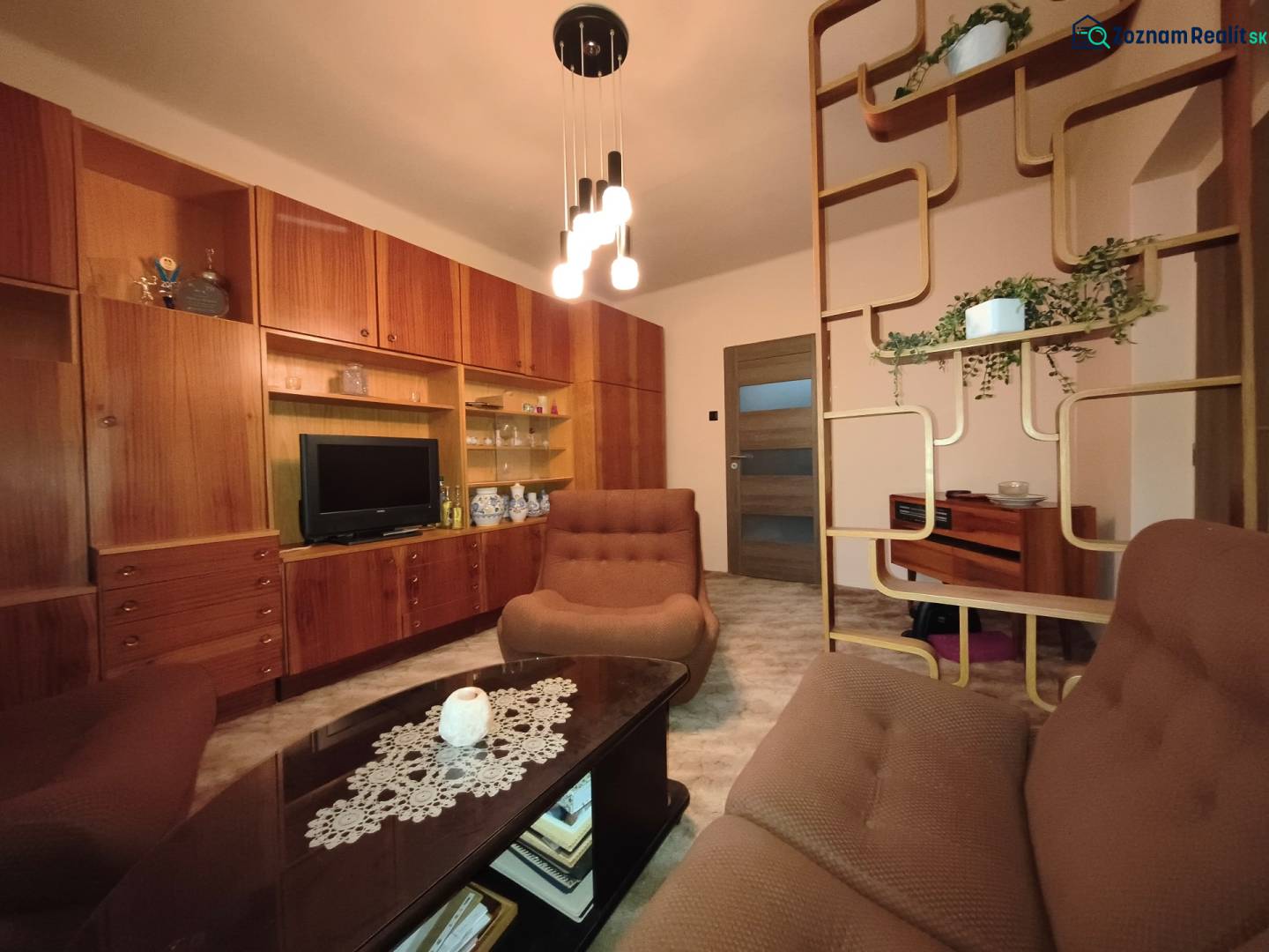 Living room in a 3-room apartment with wooden furniture and decorative shelves.