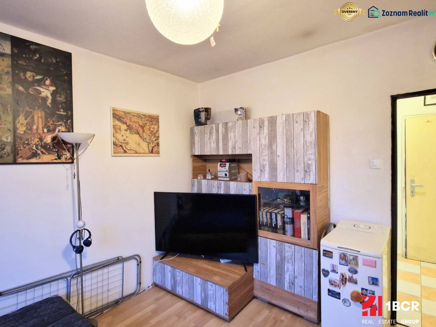 A studio apartment with wooden decor furniture, a floor lamp, and decorative paintings on the wall.