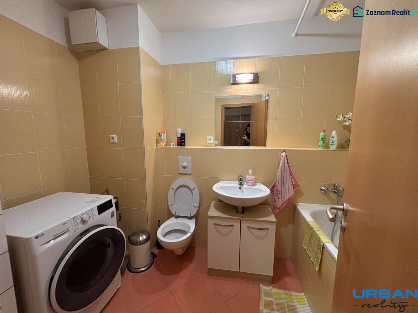 A bathroom with light tiles and a washing machine in a 2-room apartment.