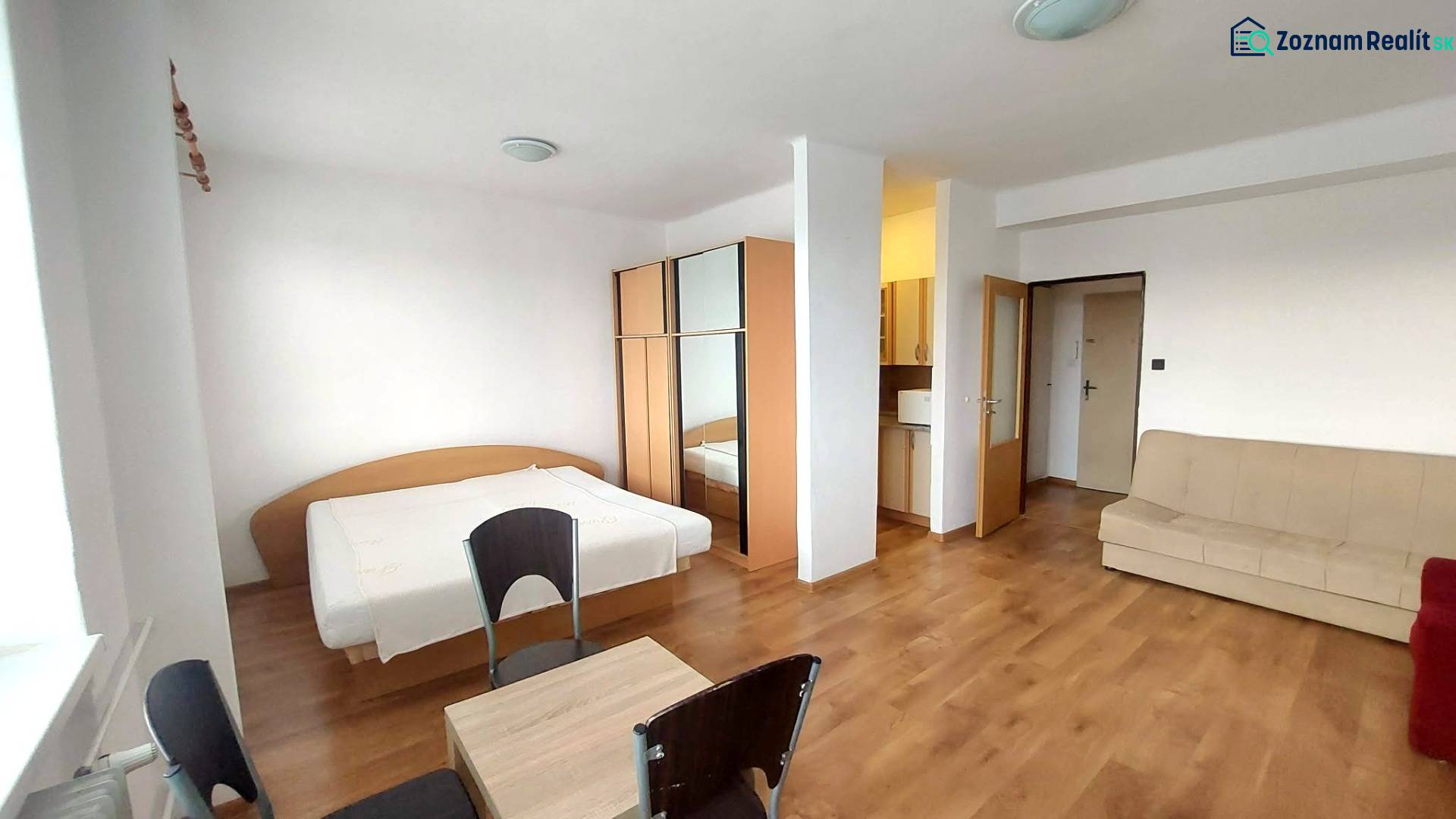 A one-room apartment with a wooden decor floor, a bed, a sofa, and a wardrobe.