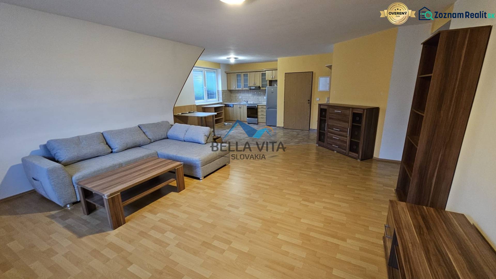 Interior with a sofa, kitchen, and wood-patterned flooring in a building.