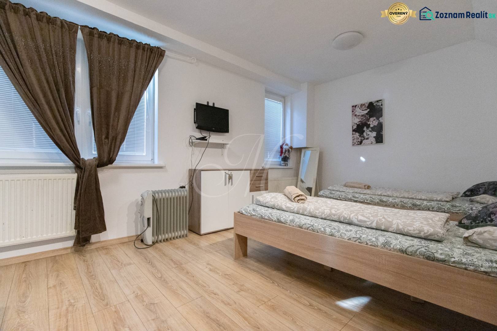 A room with beds, a television on the wall, and a floor with a wooden decor.