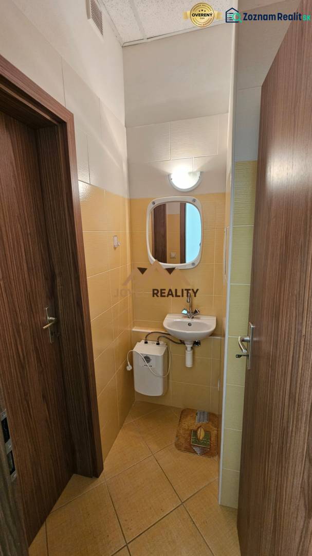A bathroom in commercial premises with a sink and a mirror, tiled with light tiles.