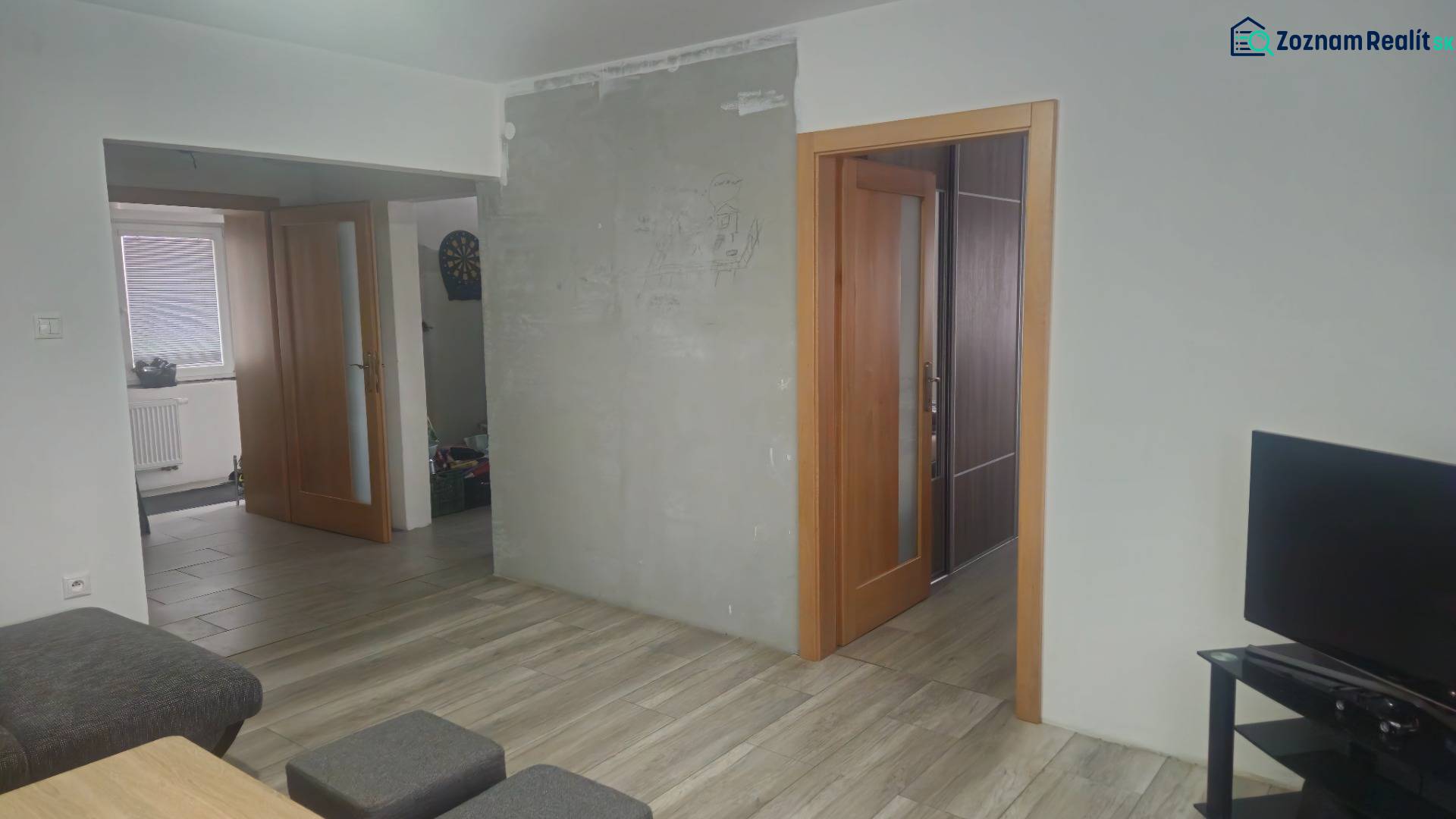 Interior of a family house with a wooden decor floor, a television, and open doors.