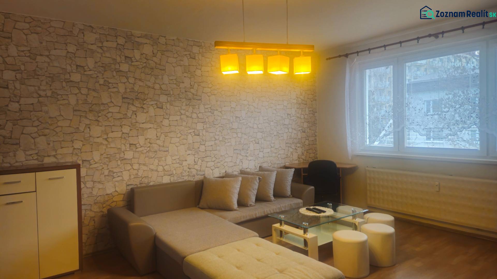 Living room with a sofa, stone cladding, wood-patterned flooring, and a large window.